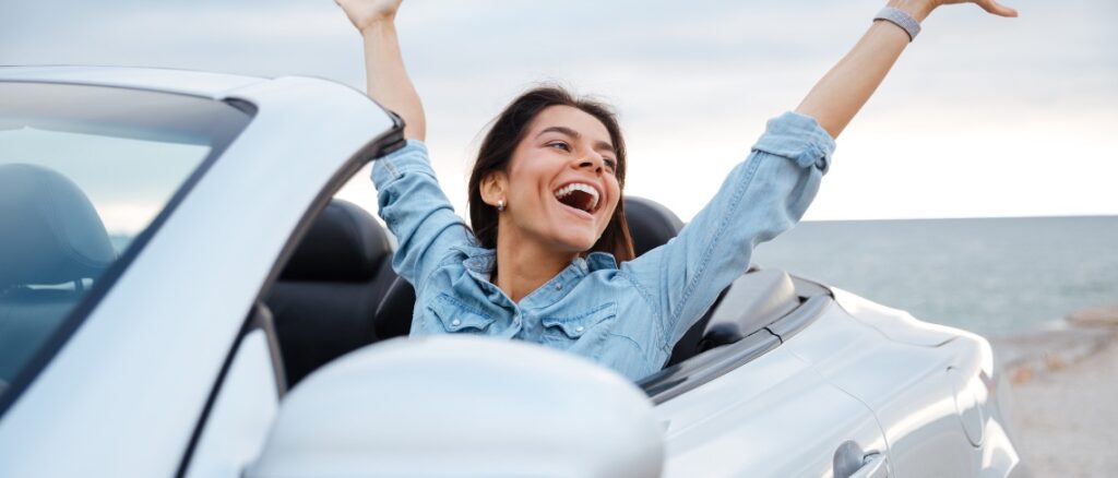 Young attractive brunette woman sitting with her hands up in cabriolet