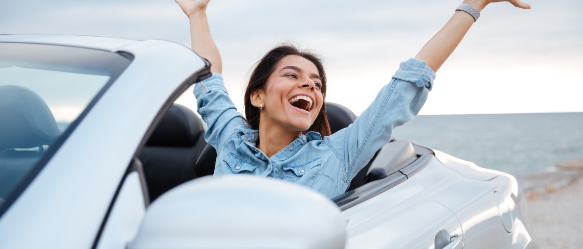 Young attractive brunette woman sitting with her hands up in cabriolet