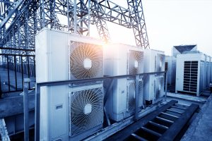 Air conditioner units (HVAC) on a roof of industrial building with blue sky and clouds in the background