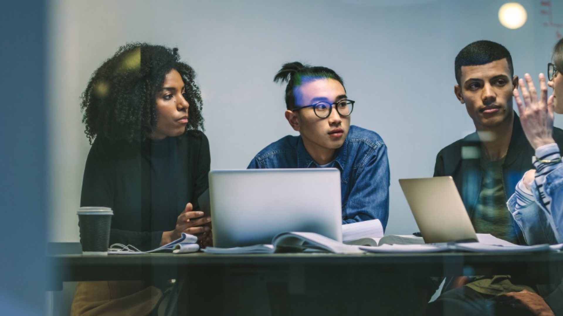Woman talking with classmates while studying together around table. Young people sitting at the table working on an assignment.