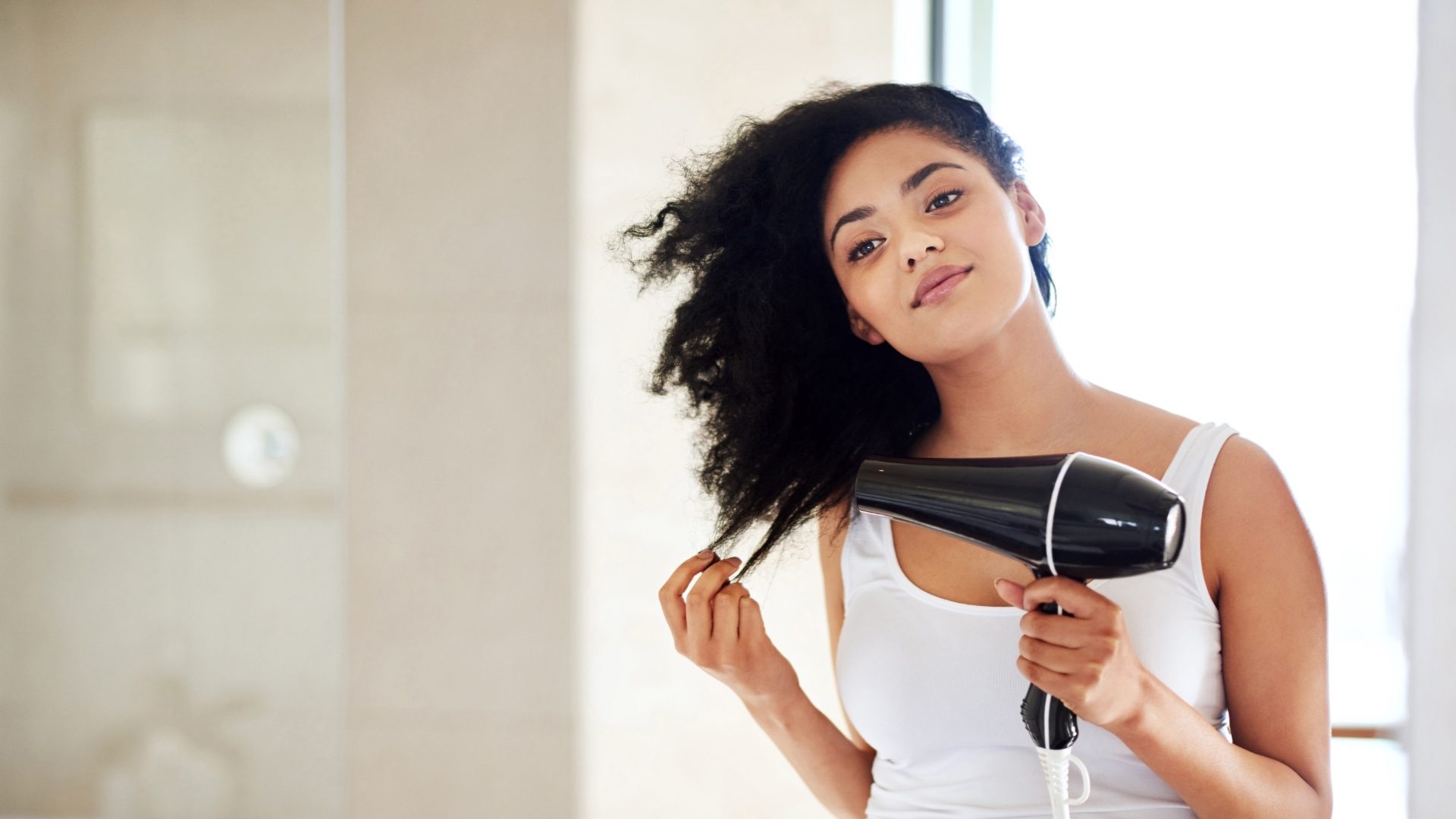 Shot of a young woman drying her hair in the bathroom