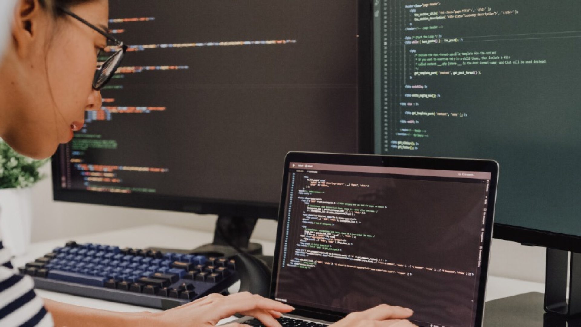 Closeup group of Asian people software developers using computer to write code sitting at desk with multiple screens at office. Programmer development concept.