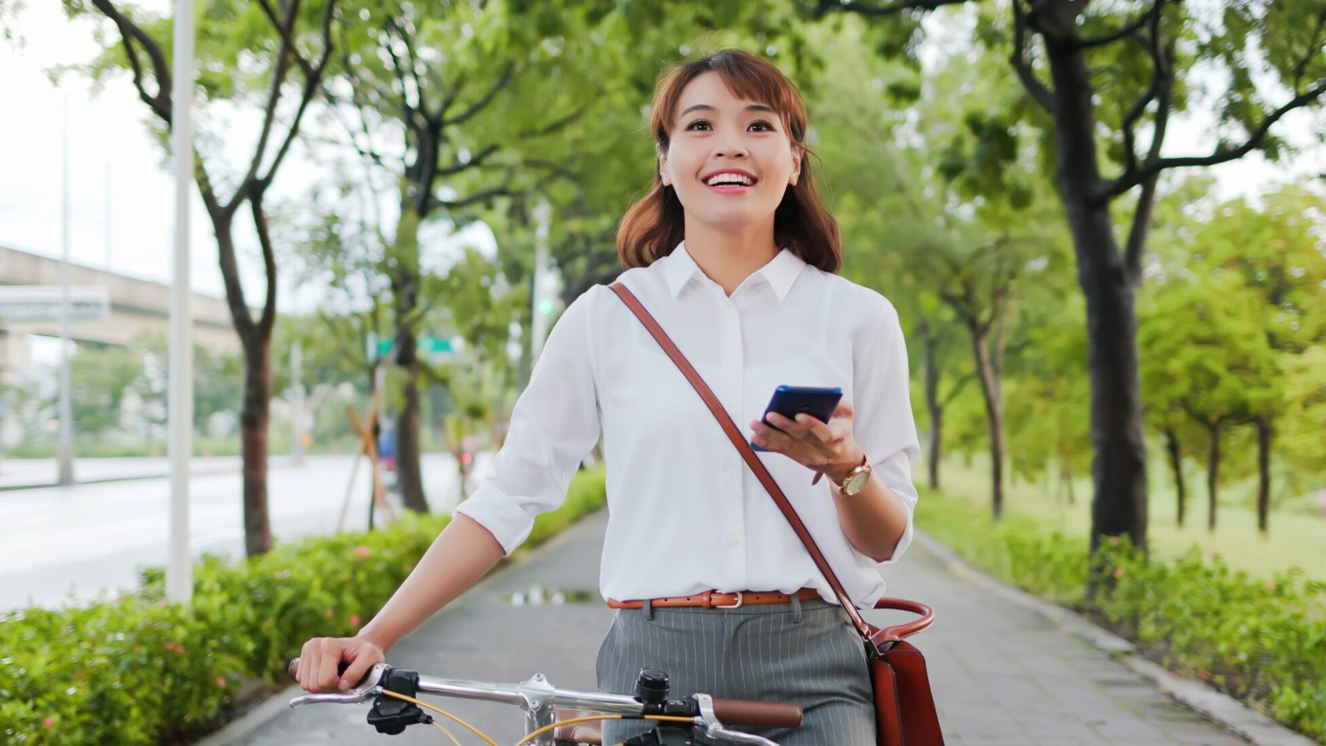 Asian businesswoman commute with her bicycle and use phone in the streets happily; Shutterstock ID 1956012232; purchase_order: 1106262587; job: ; client: ; other: