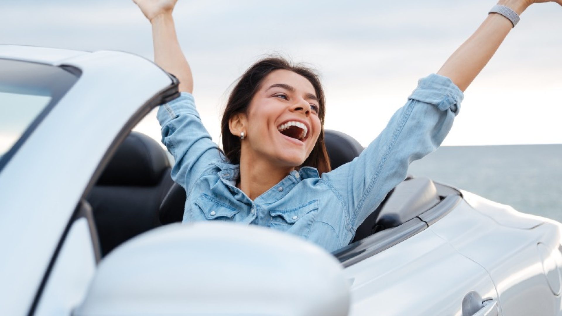 Young attractive brunette woman sitting with her hands up in cabriolet