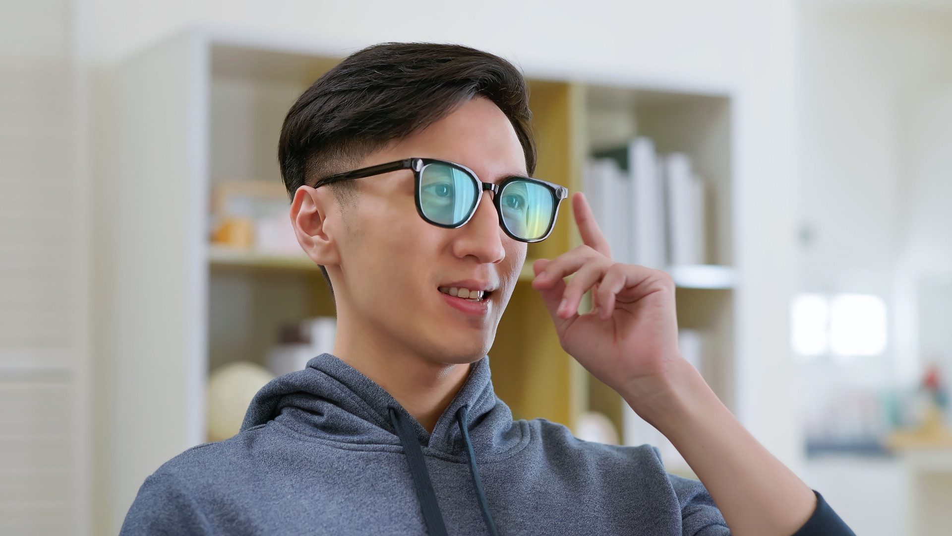 Smiling asian man wearing AR glasses seated on living room sofa surrounded by cozy home interior with shelves and books